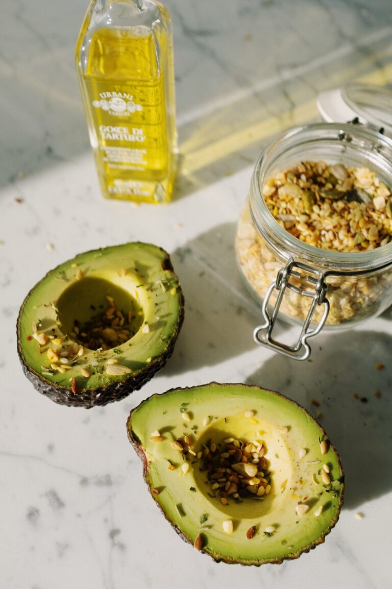 Halved avocado sprinkled with seeds alongside olive oil, representing healthy fats
