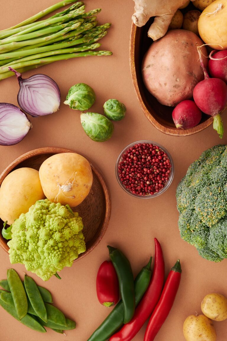 A colourful spread of fresh vegetables including broccoli, Brussels sprouts, sweet potato, radishes, romanesco, snap peas, and peppers