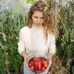 A woman in a greenhouse holding a bowl of freshly harvested organic tomatoes and peppers